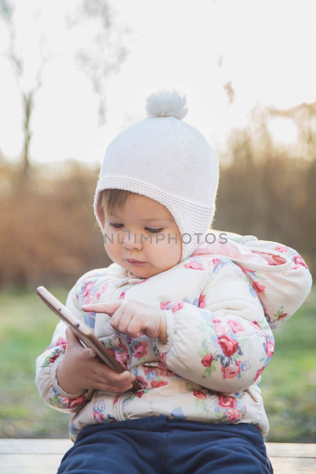 Adorable baby playing on the phone in the park.