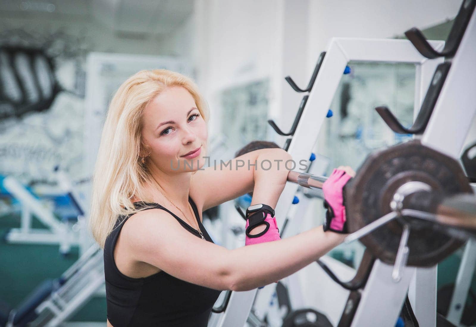 Attractive blonde stands near squat frame in gym.