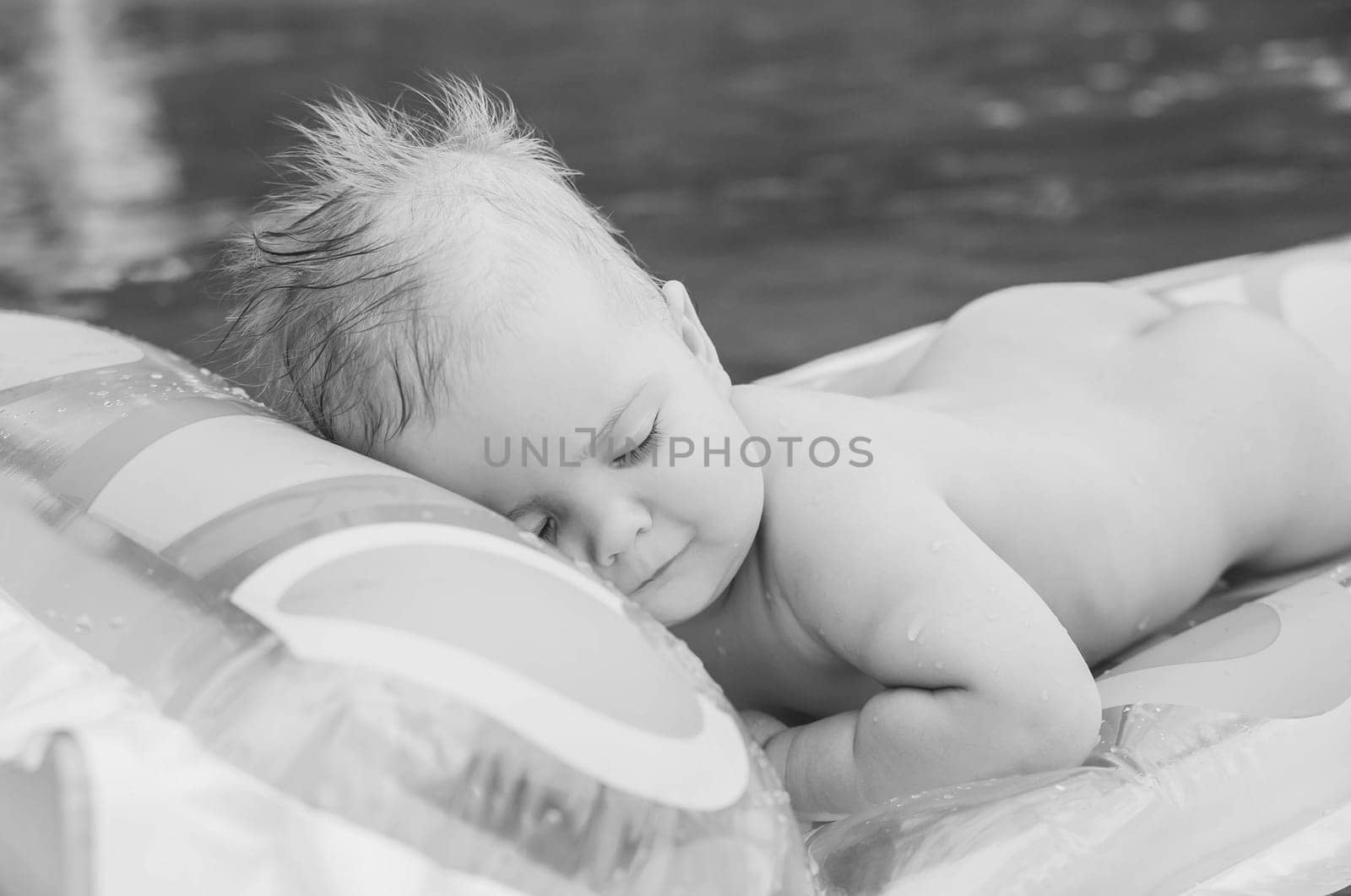 black and white photo of beautiful baby floating on air mattress on the river