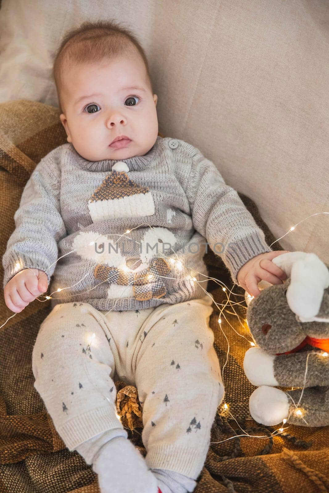 blonde baby lies on a sofa with a garland and a stuffed toy.