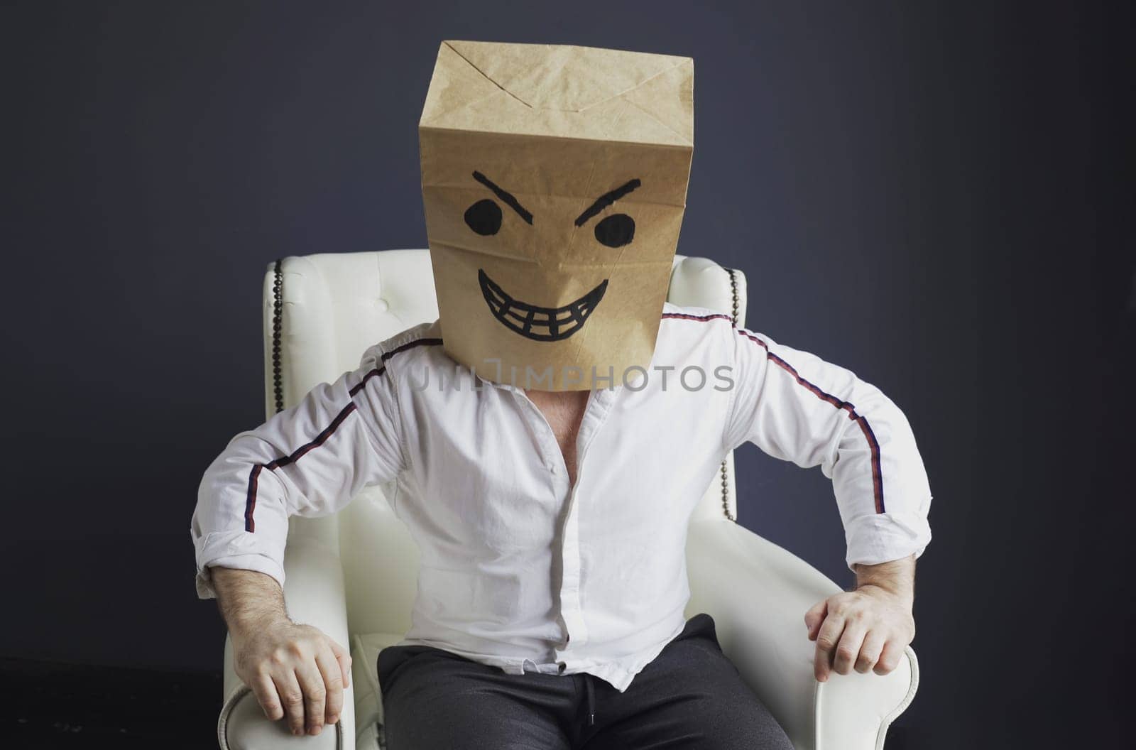 A man with a paper bag on his head, with a drawn angry smiley face, sits in a white chair. Emotions and gestures.