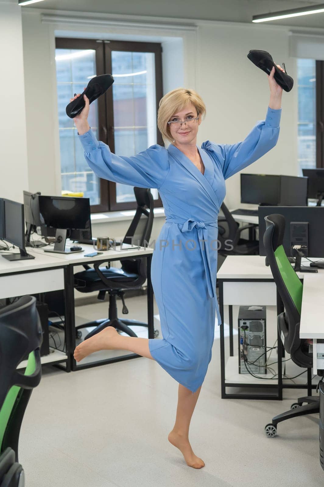 Caucasian business woman stands barefoot with shoes in her hands among the office