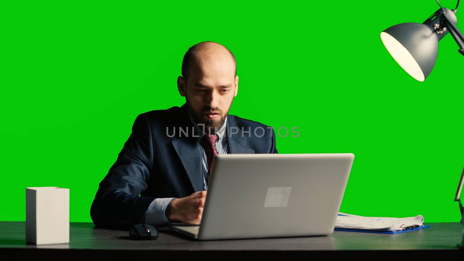 Team leader analyzing papers sitting over green screen, working with laptop and taking notes on papers. Caucasian businessman posing over isolated mockup backdrop, chroma key space.