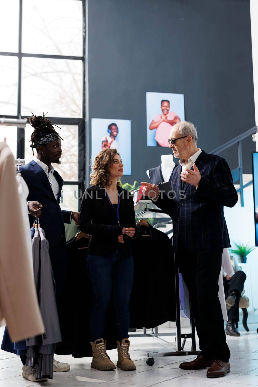 Diverse showroom employees helping senior customer choosing shirt for formal wear in shopping centre. Elderly client buying elegant clothes and fashionable accessories in modern boutique