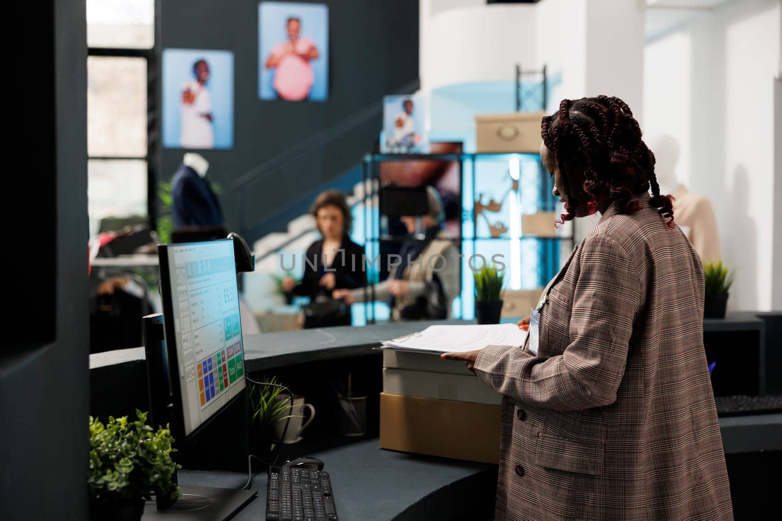 African american employee standing at cash register, checking merchandise inventory on computer in shopping centre. Showroom employee preparing packages with fashionable clothes for clients