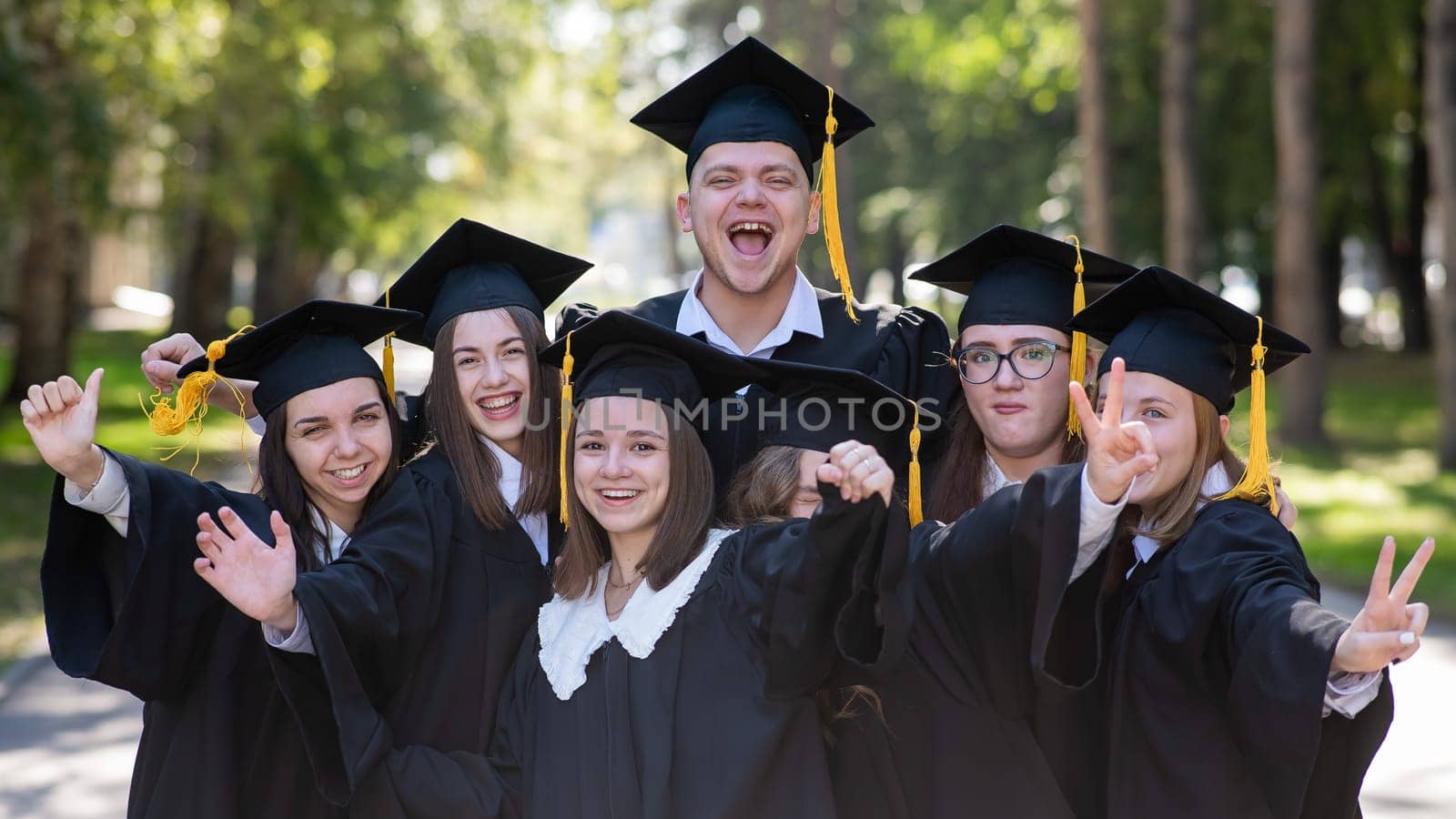 Group of happy young people in graduation gowns outdoors. Students are walking in the park. by mrwed54