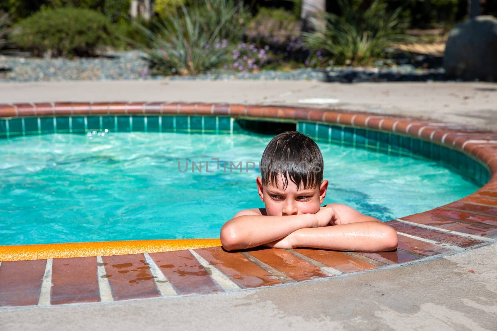 Concept of fun, health and vacation. Oudoor summer activity. A sad boy eight years old in swimming goggles is holding onto the side of the pool on a hot summer day.