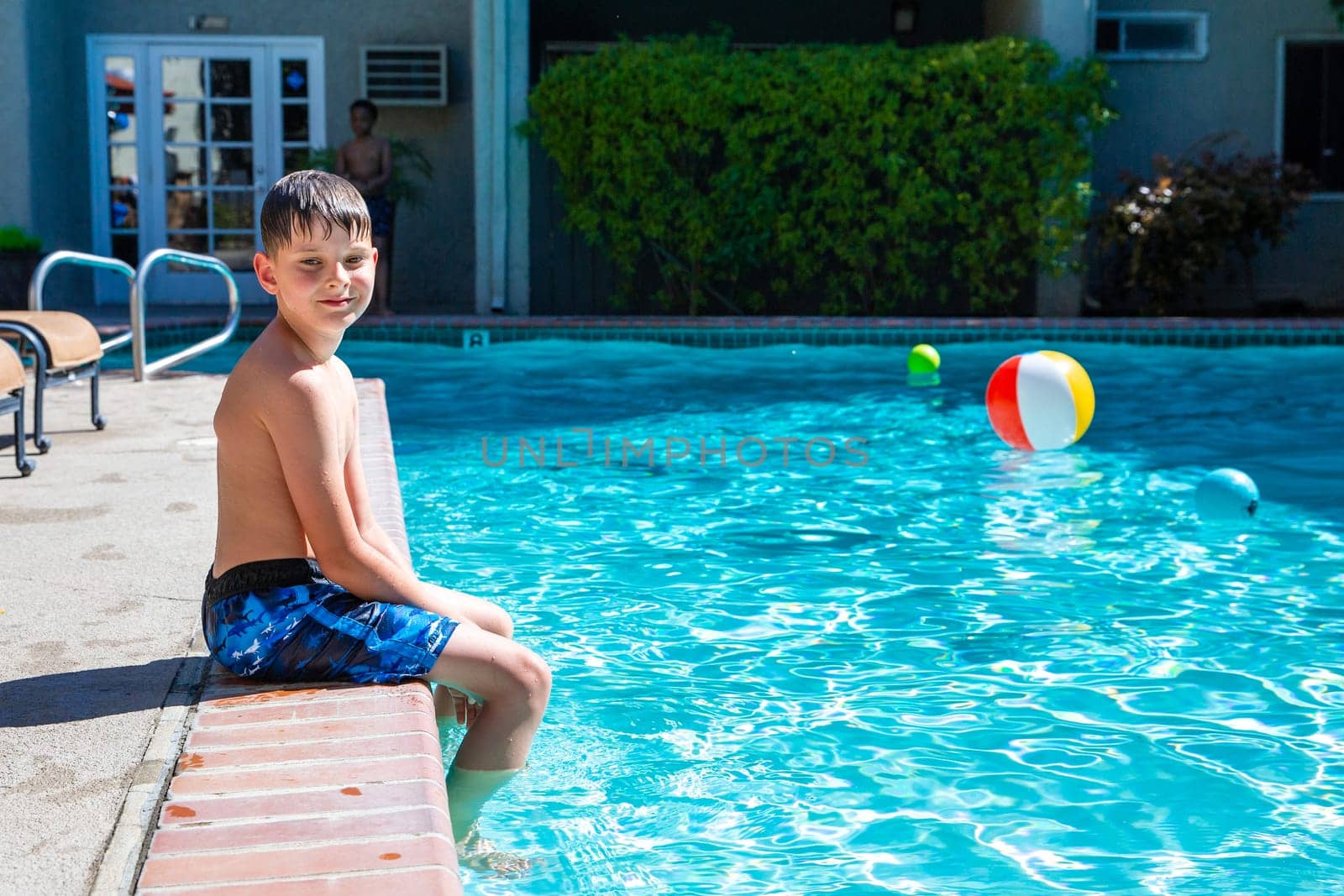 Concept of fun, health and vacation. Oudoor summer activity. Boy eight years old sits near a pool in hot summer day.