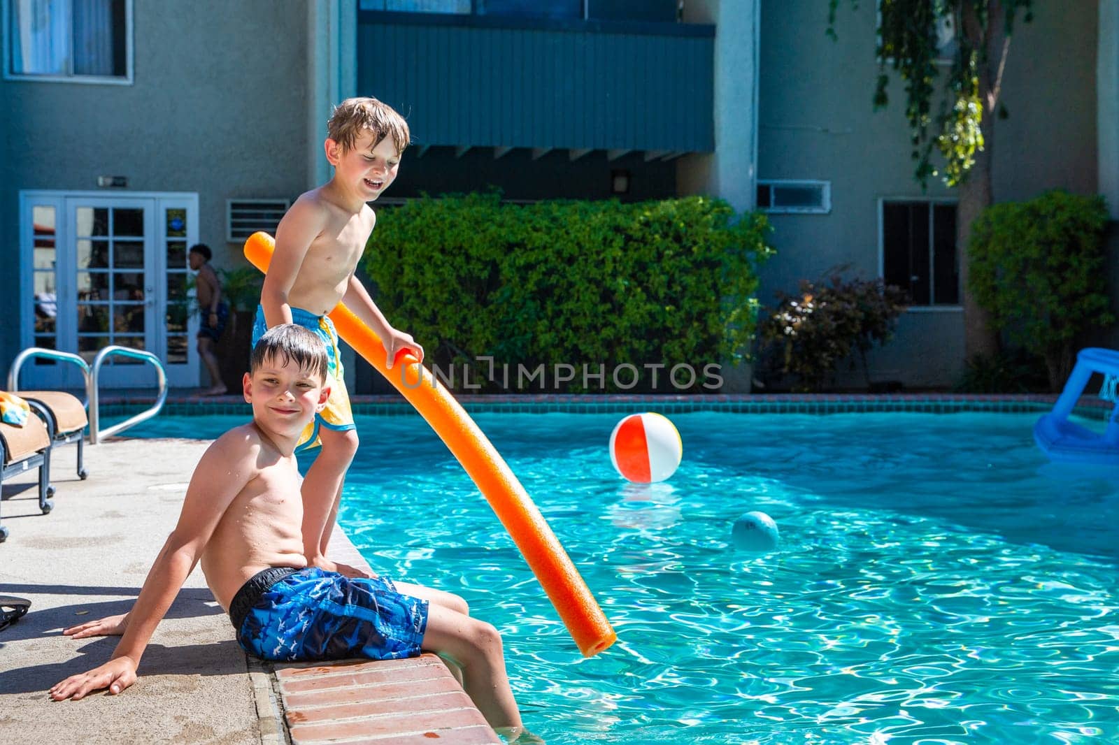 Concept of fun, health and vacation. Oudoor summer activity. Brothers boys eight and five years old with noodle sits near a pool in hot summer day.