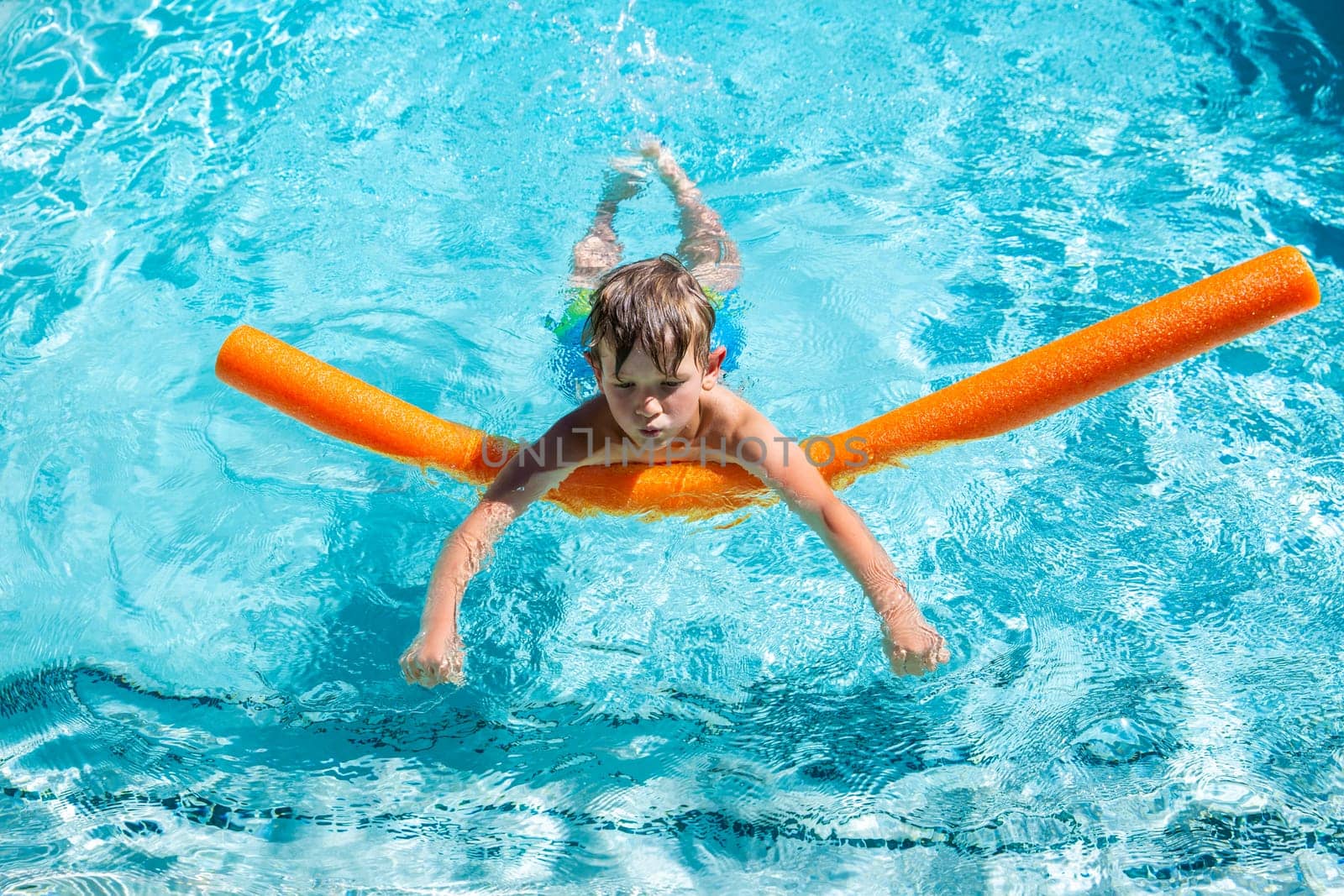 Oudoor summer activity. Concept of fun, health and vacation. A happy boy five years old is learning to swim with noodle in the pool on a hot summer day. by Marina-A