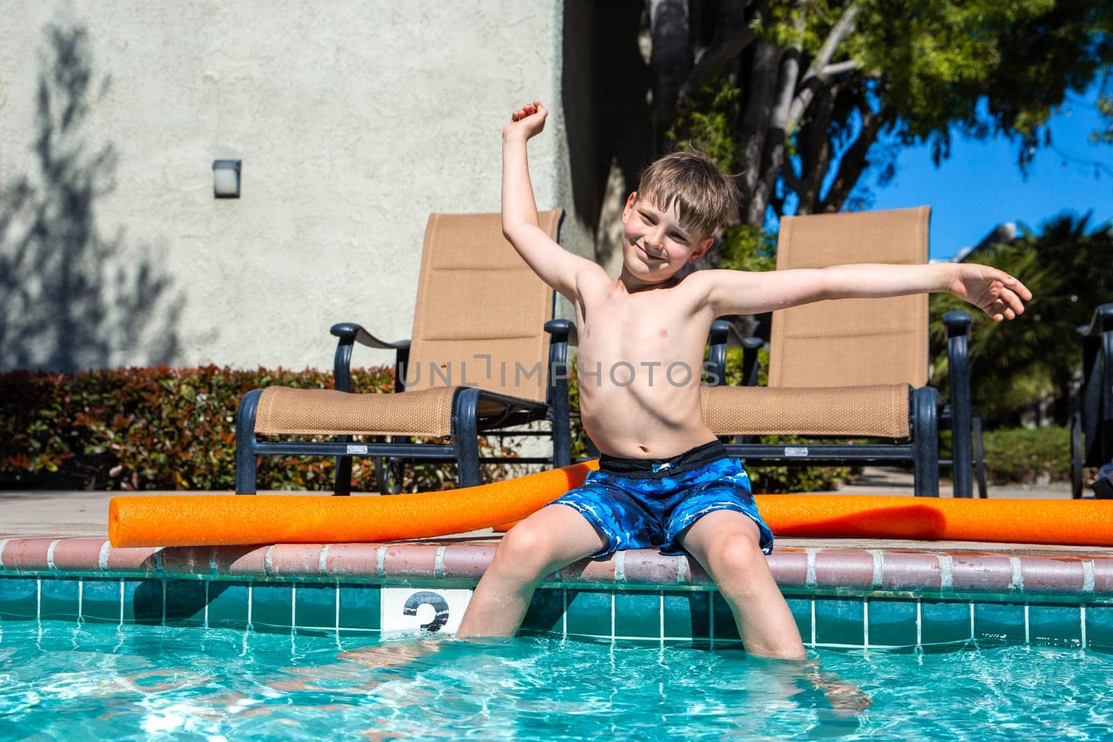 Oudoor summer activity. Concept of fun, health and vacation. Boy eight years old sits near a pool in hot summer day. by Marina-A