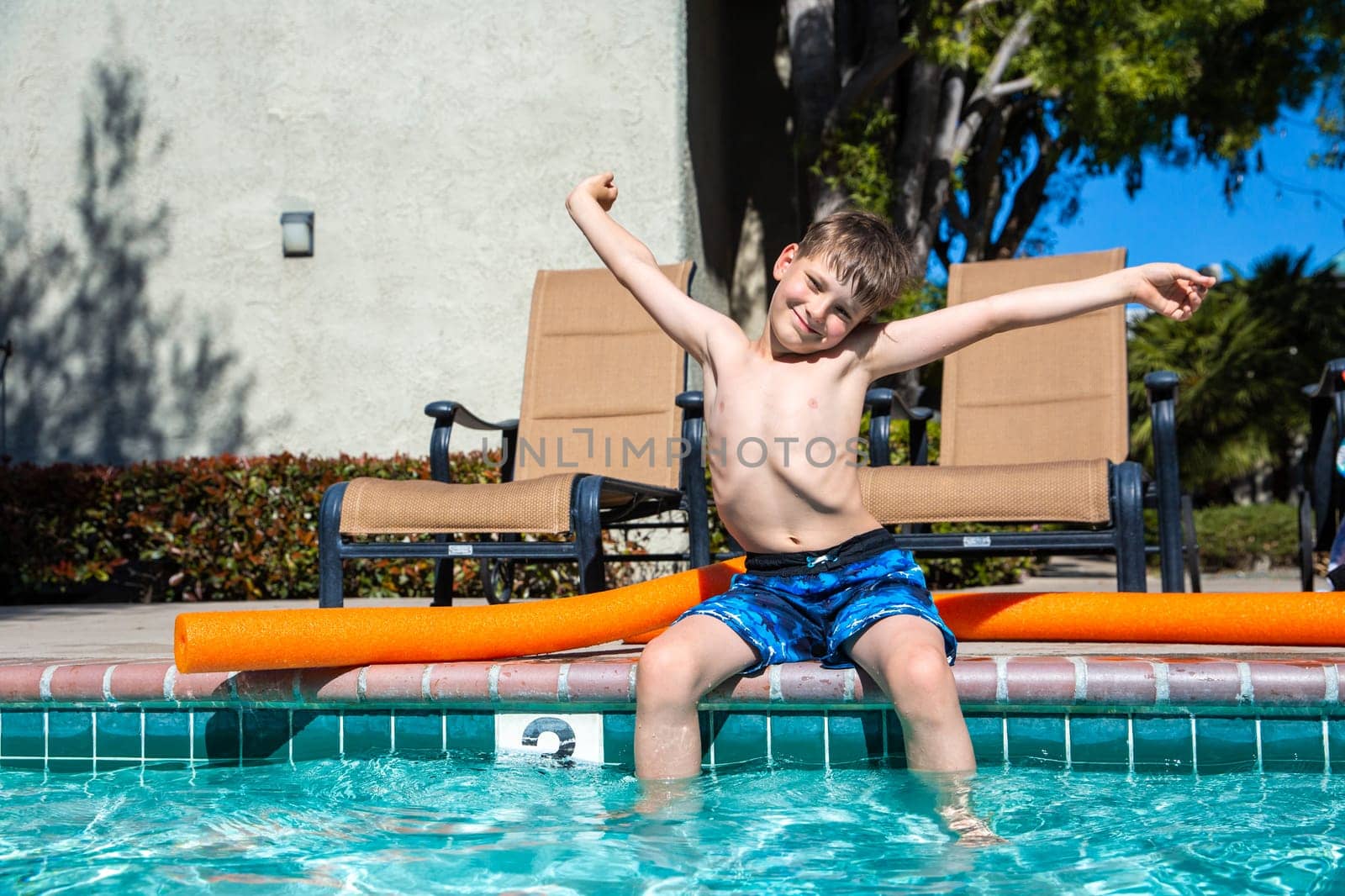 Oudoor summer activity. Concept of fun, health and vacation. Boy eight years old sits near a pool in hot summer day. by Marina-A