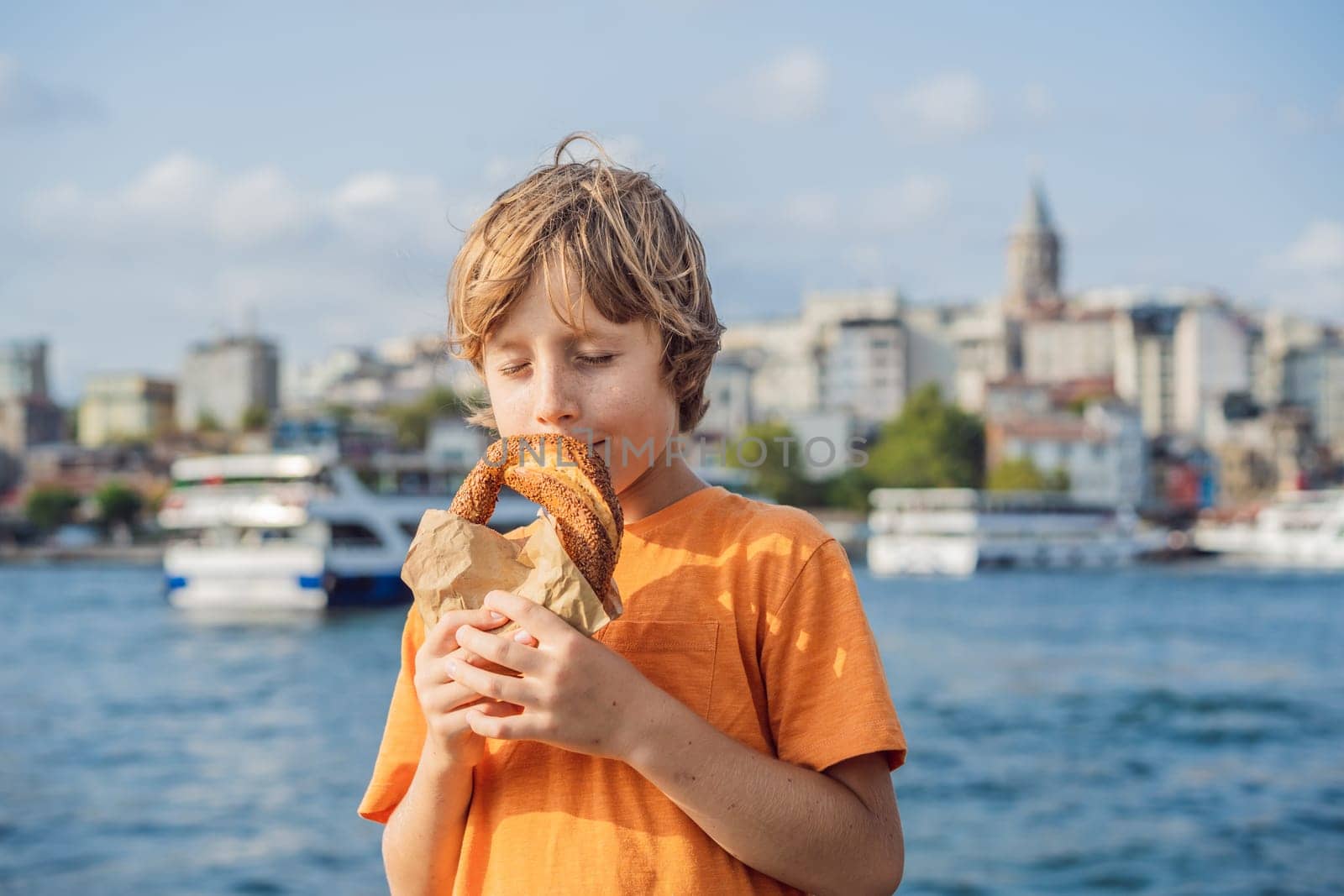 Boy in Istanbul having breakfast with Simit and a glass of Turkish tea. Glass of Turkish tea and bagel Simit against golden horn bay and the Galata Tower in Istanbul, Turkey. Turkiye. Traveling with kids concept.