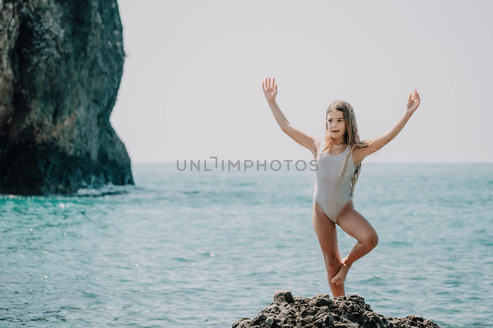 Woman and her daughter practicing balancing yoga pose on one leg up together on rock in the sea. Silhouette mother and daughter doing yoga at beach by panophotograph