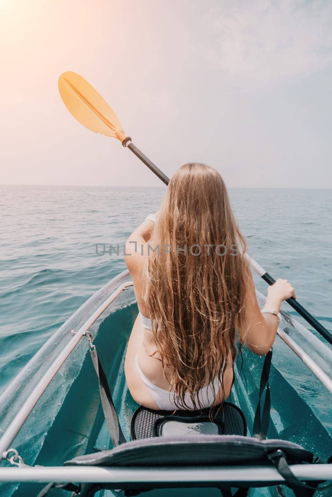 Woman in kayak back view. Happy young woman with long hair floating in transparent kayak on the crystal clear sea. Summer holiday vacation and cheerful female people relaxing having fun on the boat by panophotograph