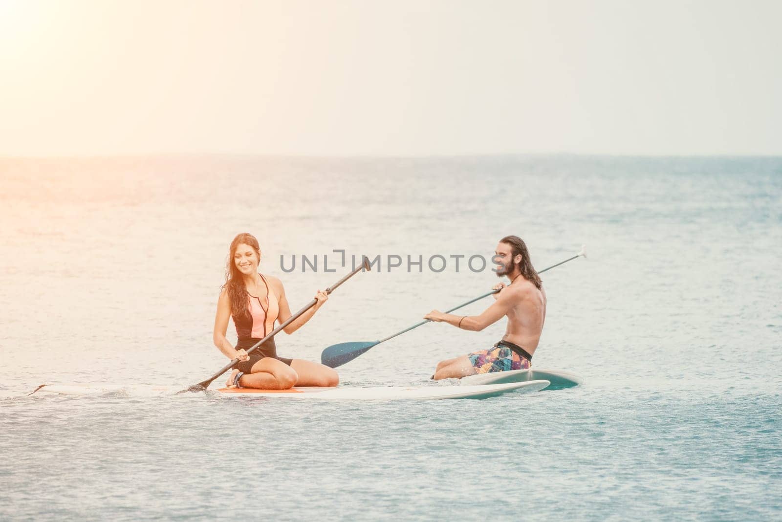 Sea woman and man on sup. Silhouette of happy young woman and man, surfing on SUP board, confident paddling through water surface. Idyllic sunset. Active lifestyle at sea or river