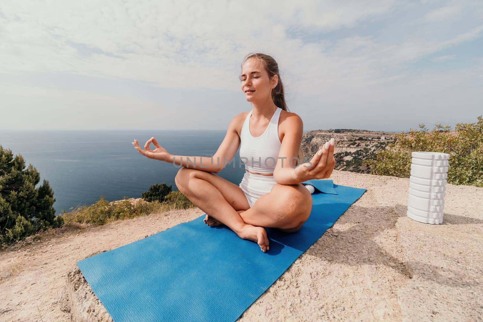 Middle aged well looking woman with black hair doing Pilates with the ring on the yoga mat near the sea on the pebble beach. Female fitness yoga concept. Healthy lifestyle, harmony and meditation.