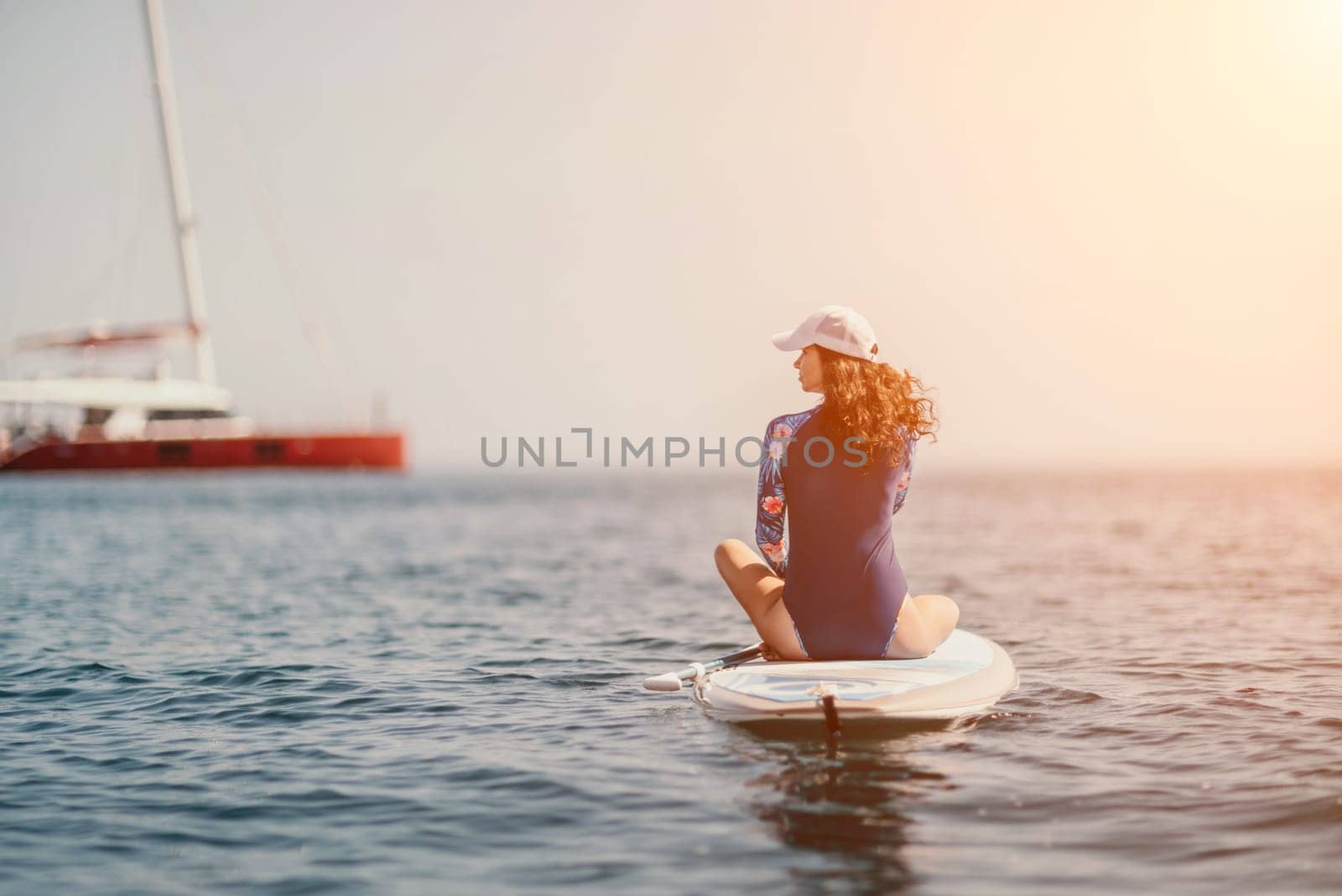 Woman sup yoga. Middle age sporty woman practising yoga pilates on paddle sup surfboard. Female stretching doing workout on sea water. Modern individual female hipster outdoor summer sport activity. by panophotograph