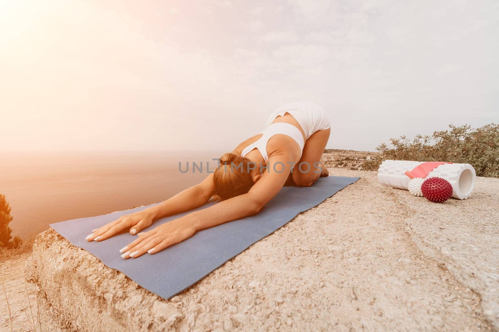 Woman sea pilates. Sporty, middle-aged woman practicing pilates in park near the sea. trains on a yoga mat and exudes a happy and active demeanor. healthy lifestyle through exercise and meditation. by panophotograph