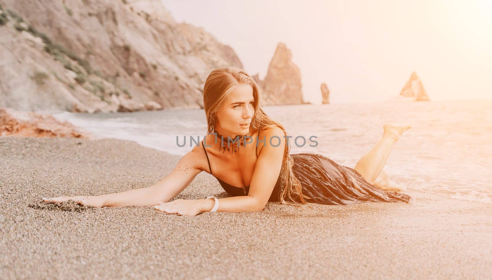 Woman summer travel sea. Happy tourist in black dress enjoy taking picture outdoors for memories. Woman traveler posing on sea beach surrounded by volcanic mountains, sharing travel adventure journey by panophotograph