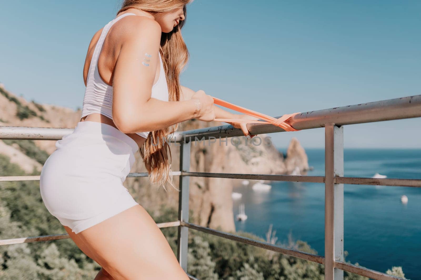 Young woman with black hair, fitness instructor in pink sports leggings and tops, doing pilates on yoga mat with magic pilates ring by the sea on the beach. Female fitness daily yoga concept