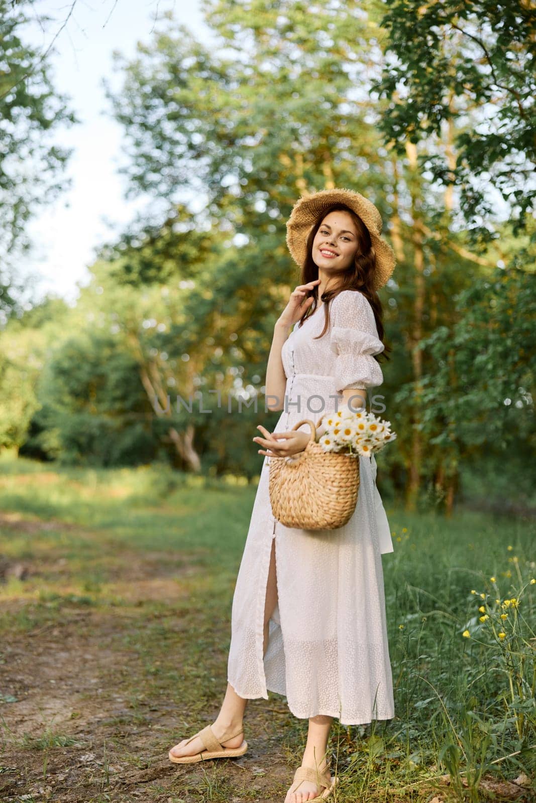 a woman in a light summer dress and a wicker hat stands in the forest with a basket of daisies in her hands. High quality photo