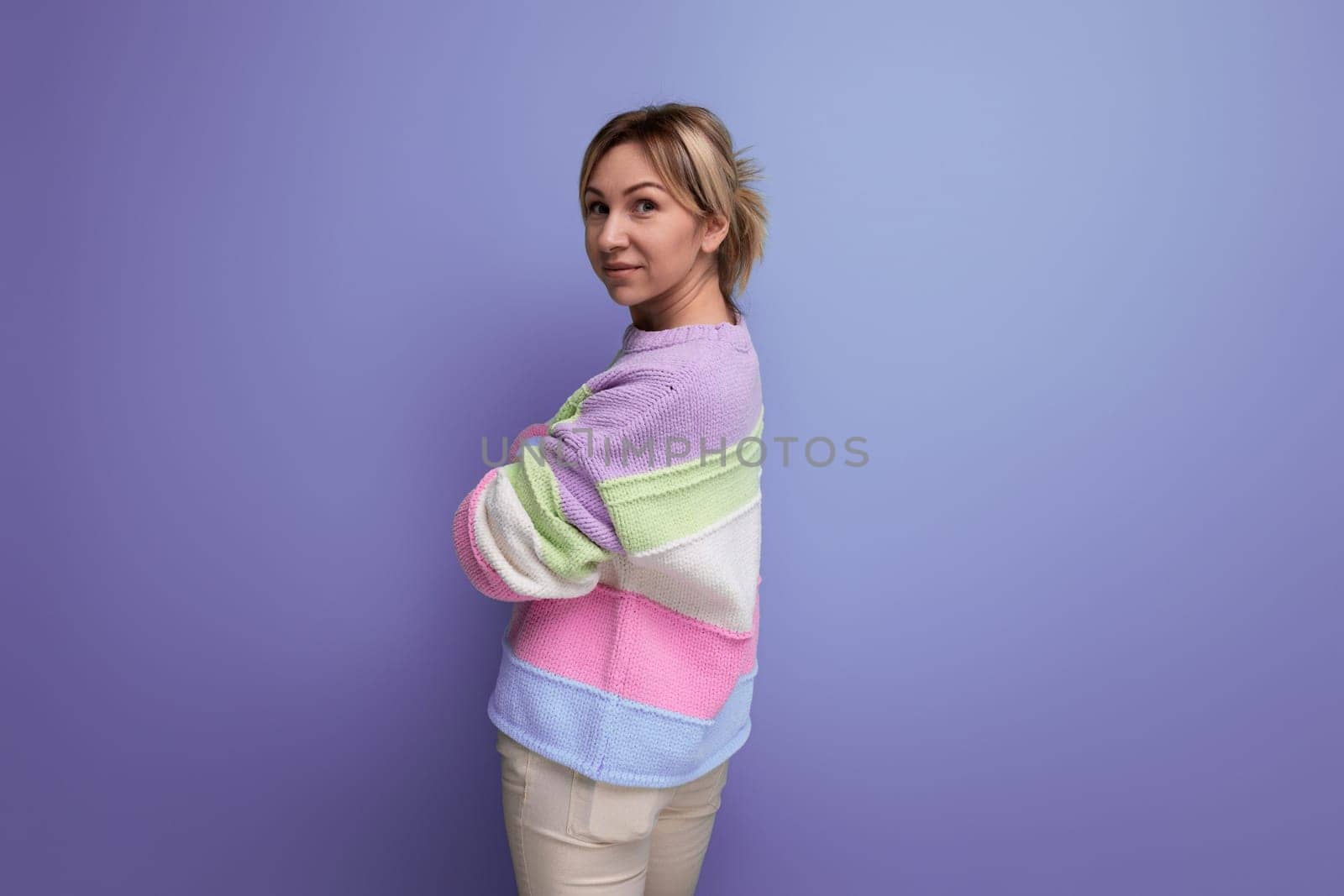 attractive blond young woman standing sideways on purple background with copy space.