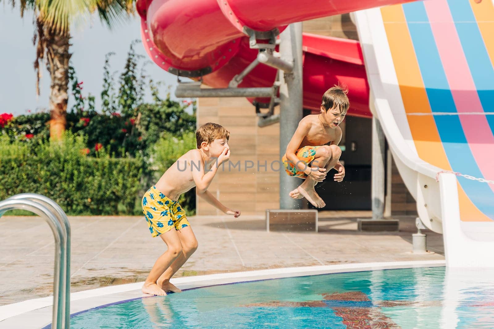 Two brothers Childs jumping and playing in swimming pool at sunny day. Kids friends boys refreshing at heat weather, active vacation and healthy lifestyle. Happy summer.