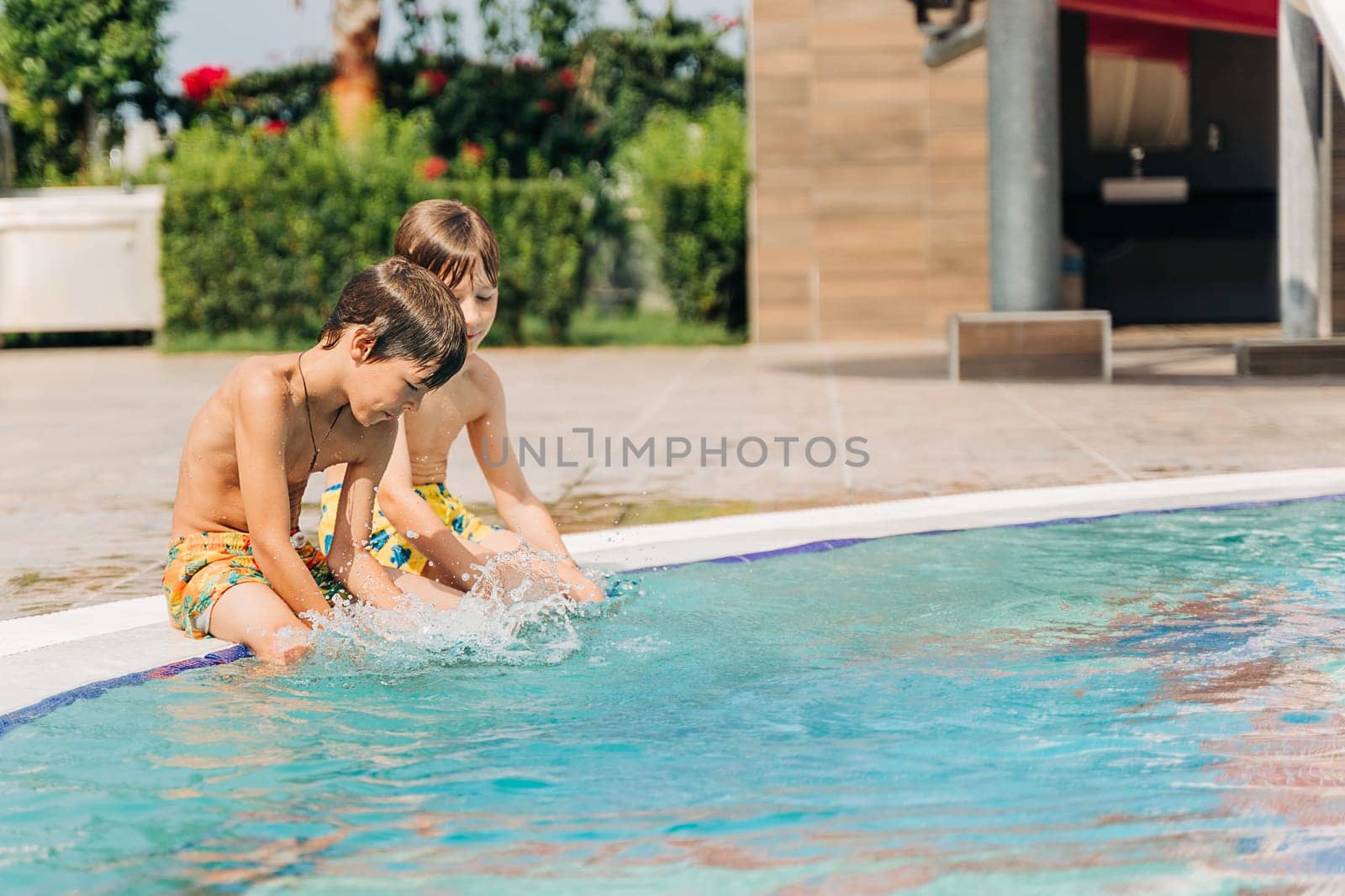 Two brothers Childs laughing while playing in swimming pool at sunny day. Kids friends boys refreshing at heat weather, active vacation and healthy lifestyle. Happy summer.