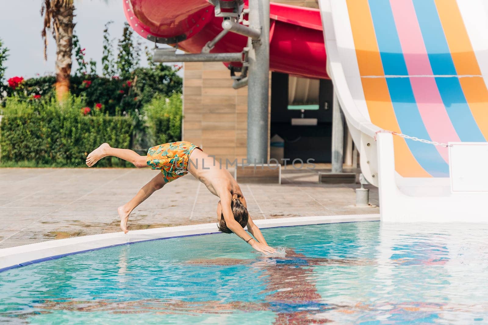 Child jumping and dives in swimming pool at sunny day. Kid boy refreshing and playing at heat weather, active vacation and healthy lifestyle. Happy summer.