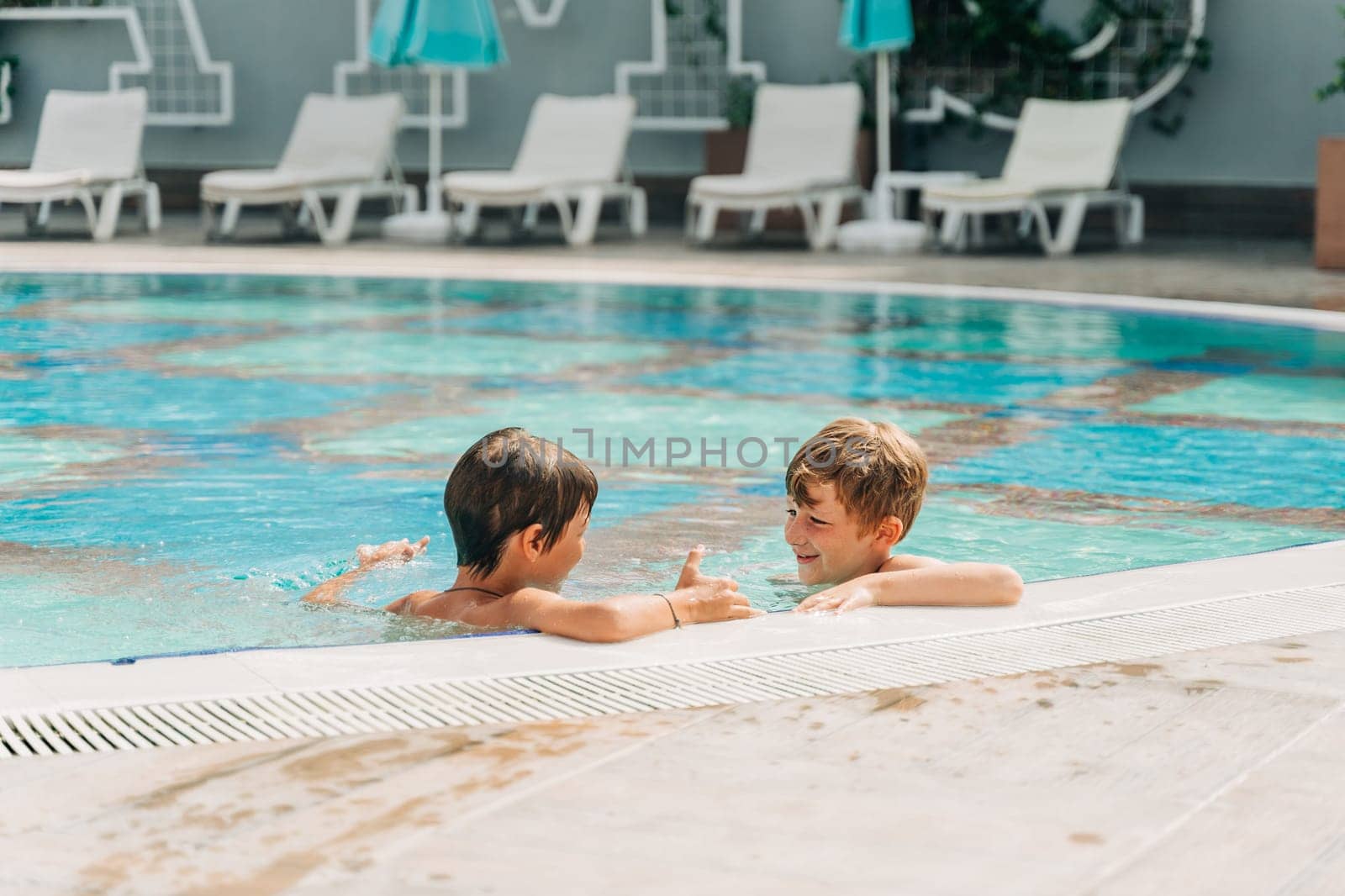 Two brothers Childs laughing while playing in swimming pool at sunny day. Kids friends boys refreshing at heat weather, active vacation and healthy lifestyle. Happy summer.