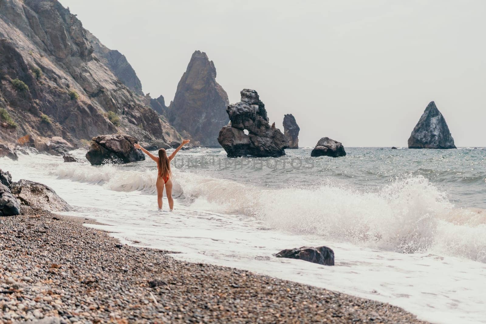 Woman travel sea. Young Happy woman in a long red dress posing on a beach near the sea on background of volcanic rocks, like in Iceland, sharing travel adventure journey