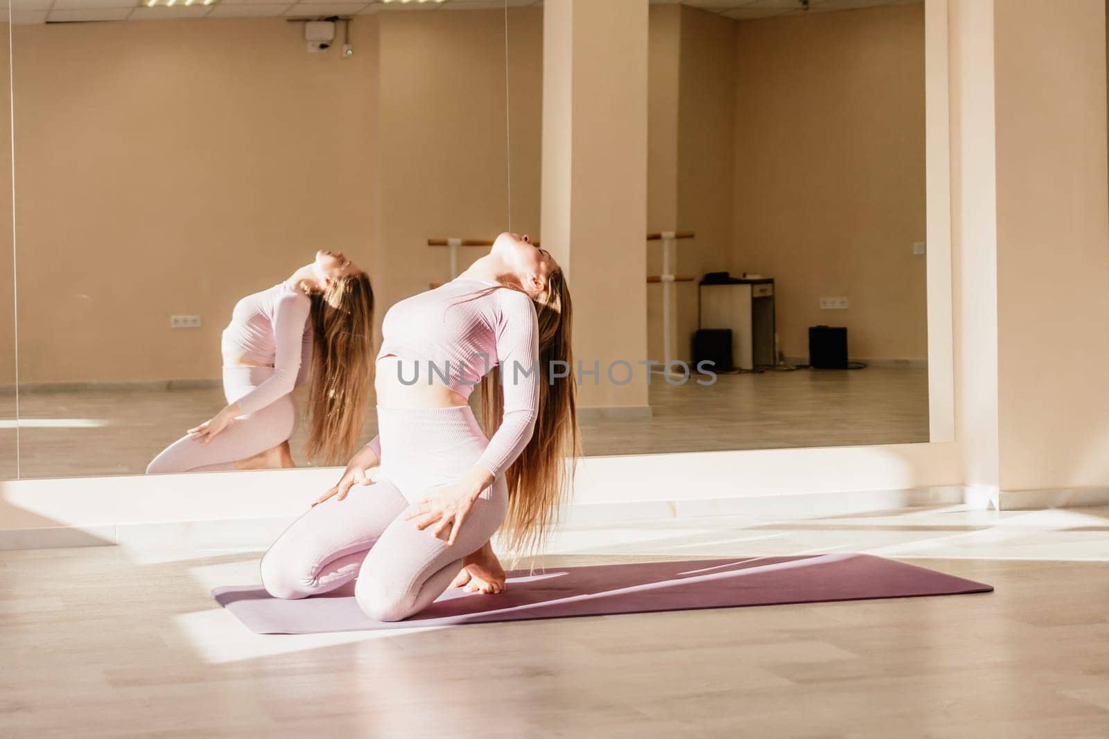 Young woman with long hair in white swimsuit and boho style braclets practicing outdoors on yoga mat by the sea on a sunset. Women's yoga fitness routine. Healthy lifestyle, harmony and meditation