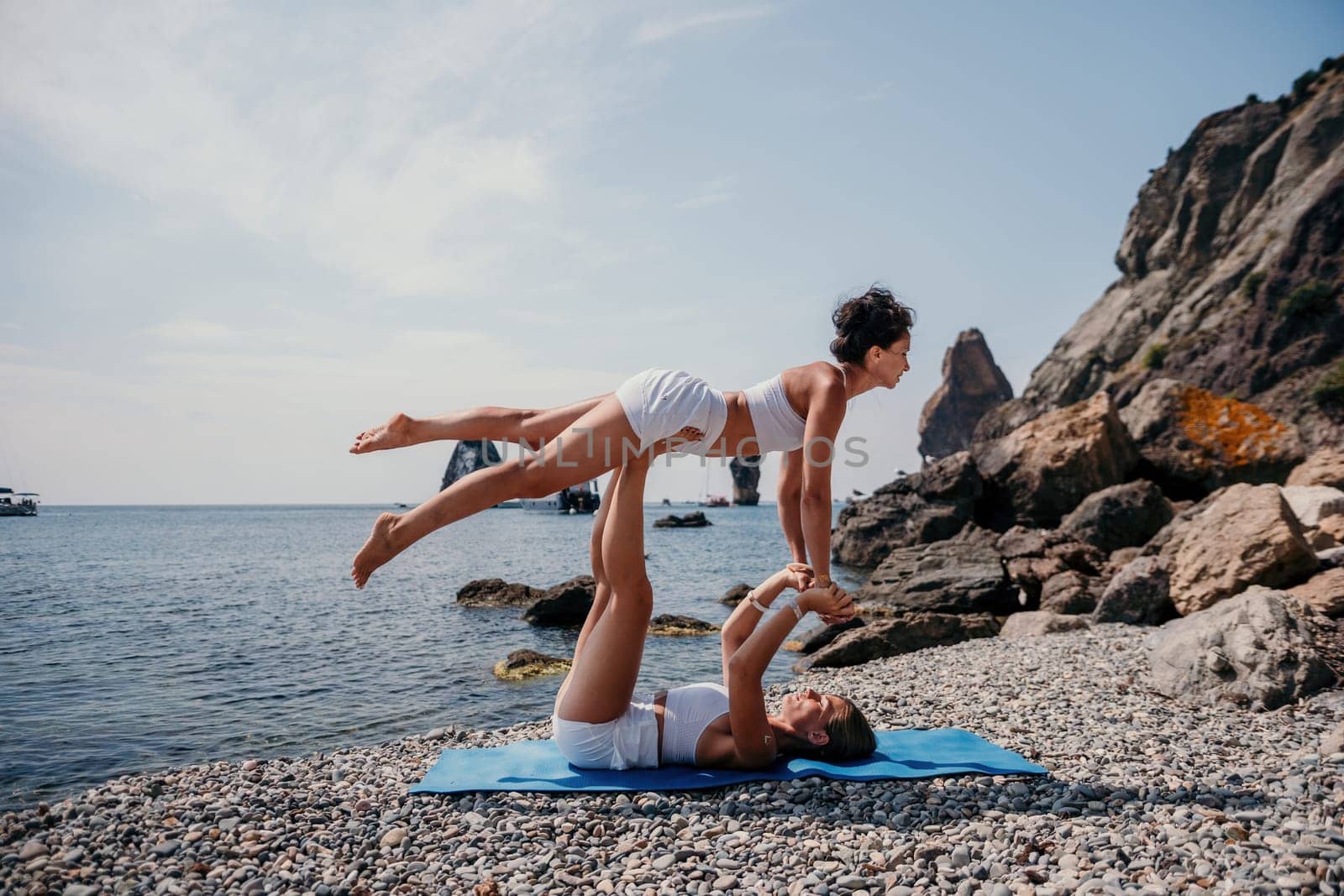 Woman sea yoga. Two Happy women meditating in yoga pose on the beach, ocean and rock mountains. Motivation and inspirational fit and exercising. Healthy lifestyle outdoors in nature, fitness concept. by panophotograph