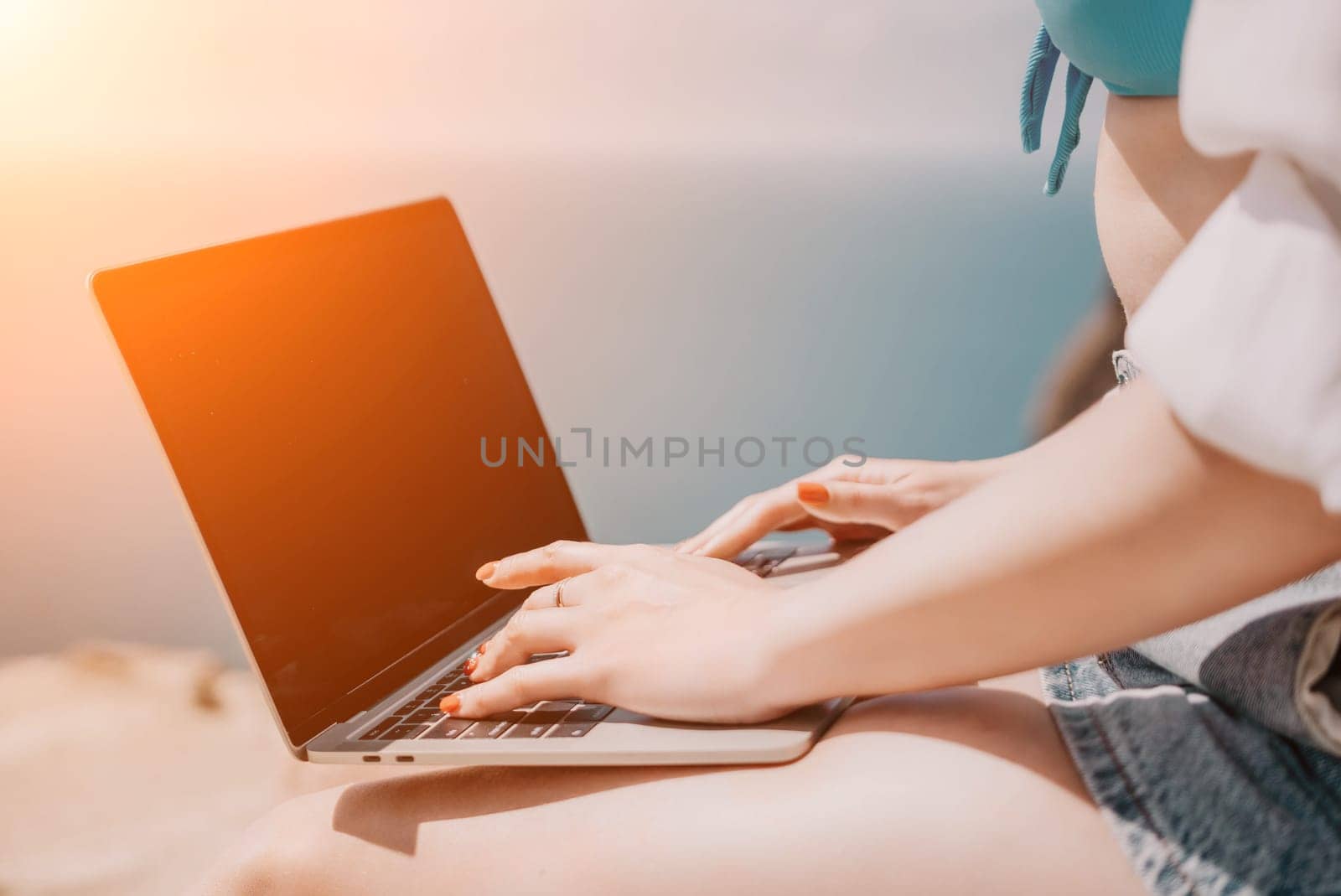 Woman sea laptop. Business woman in yellow hat working on laptop by sea. Close up on hands of pretty lady typing on computer outdoors summer day. Freelance, digital nomad, travel and holidays concept. by panophotograph