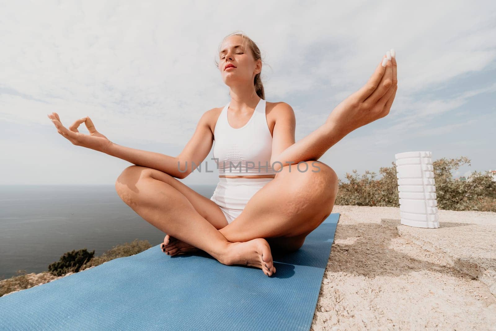 Middle aged well looking woman with black hair doing Pilates with the ring on the yoga mat near the sea on the pebble beach. Female fitness yoga concept. Healthy lifestyle, harmony and meditation.