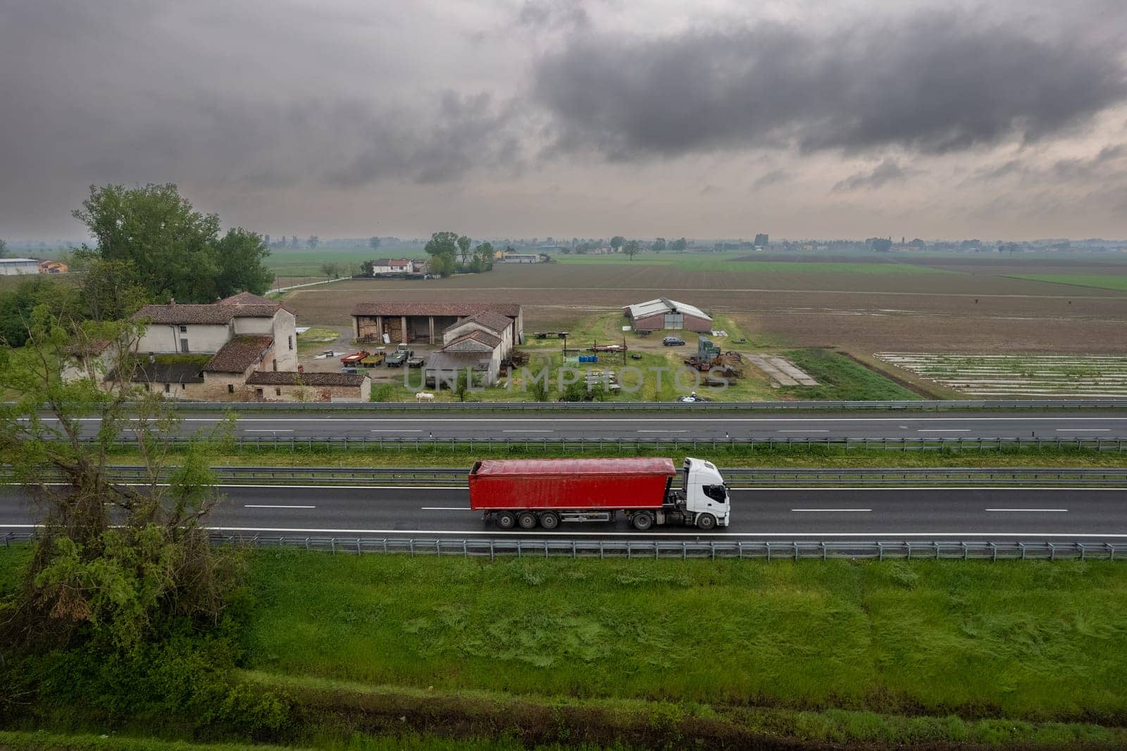 Cargo trucks and cars in the motorway a1 autostrada del sole aerial point of view in between padain plain rural fields