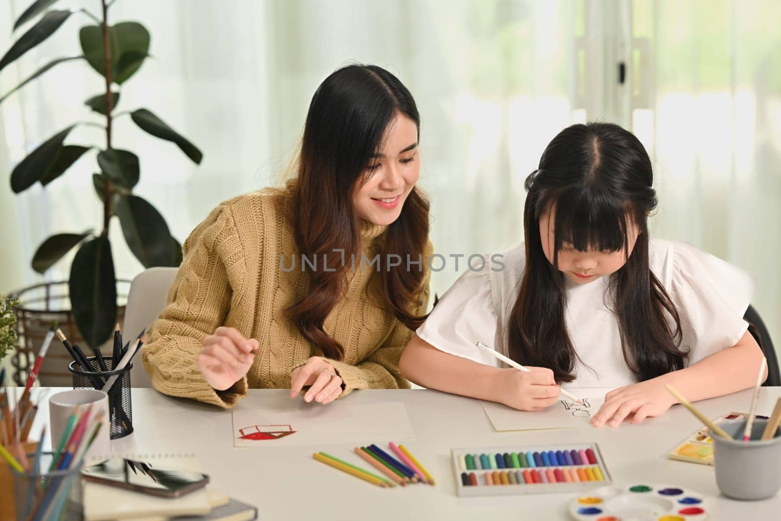 Image of mother and daughter drawing together in bright living room. Family home leisure concept.