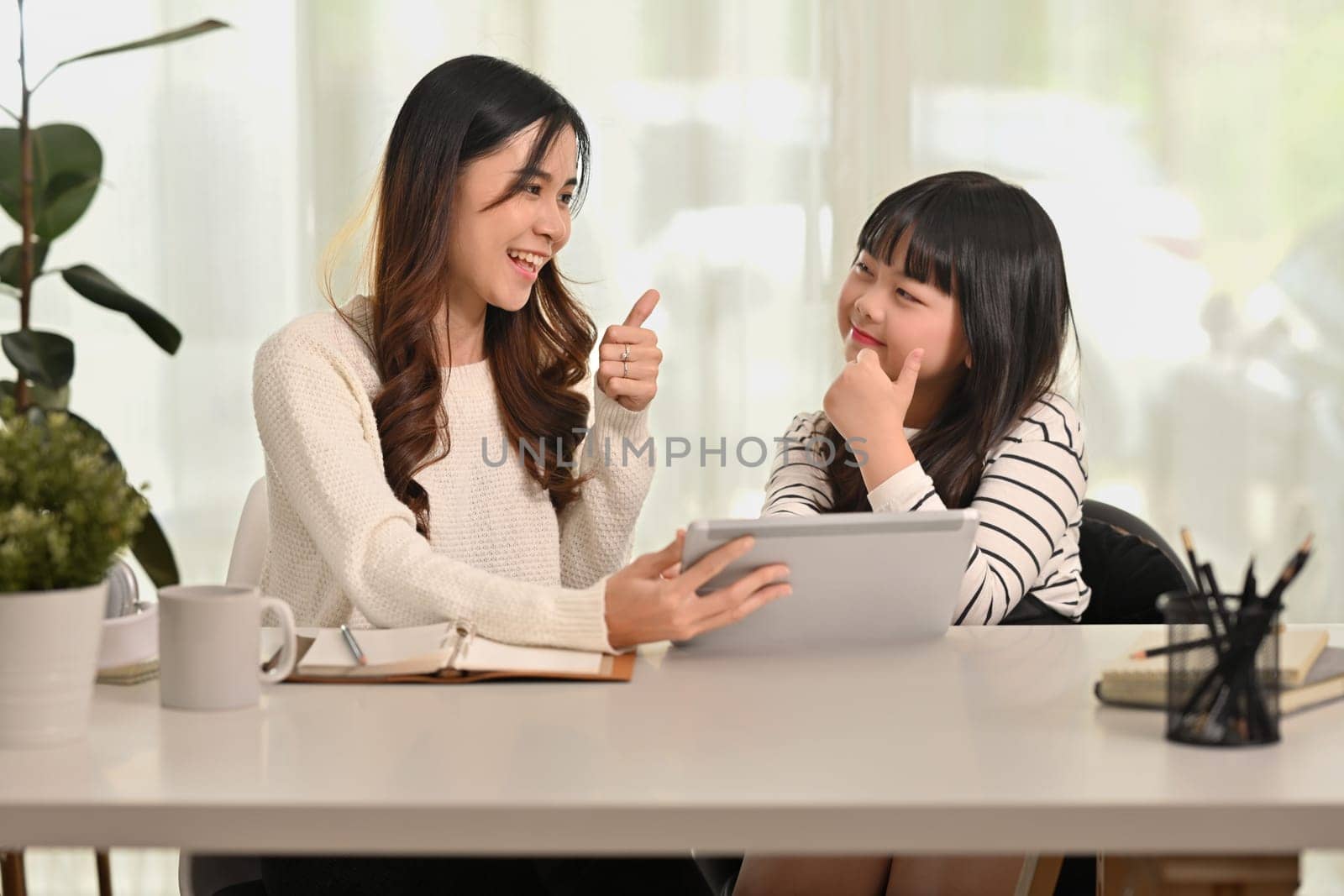 Cute little asian schoolgirl doing homework with mother at home. Distance education, homeschooling concept.