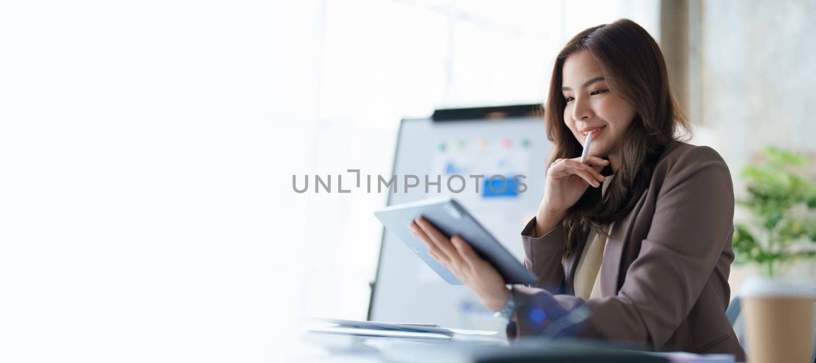 businesswoman in a black suit inside the office using tablet computer, audit paperwork for customers to contact, business people concept