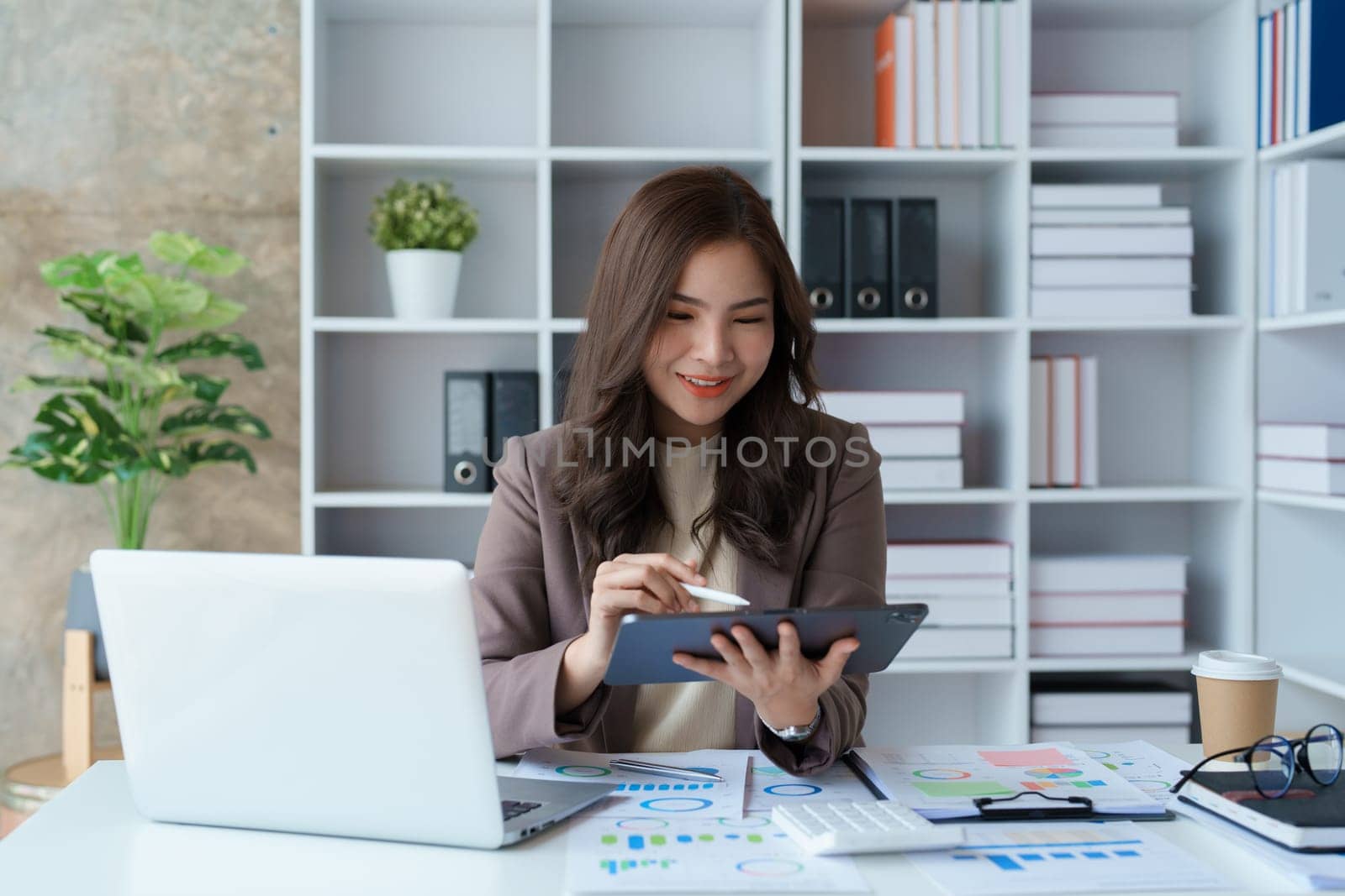 businesswoman in a black suit inside the office using tablet computer, audit paperwork for customers to contact, business people concept