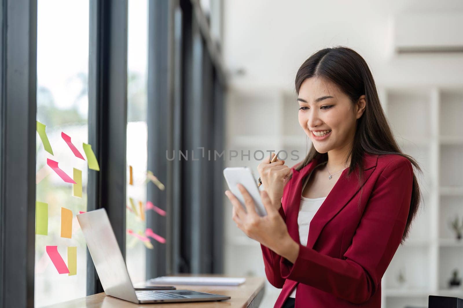 Portrait of businesswoman looks surprised and excited at smartphone screen Excited happy, sticky papers notes on glass wall in office.