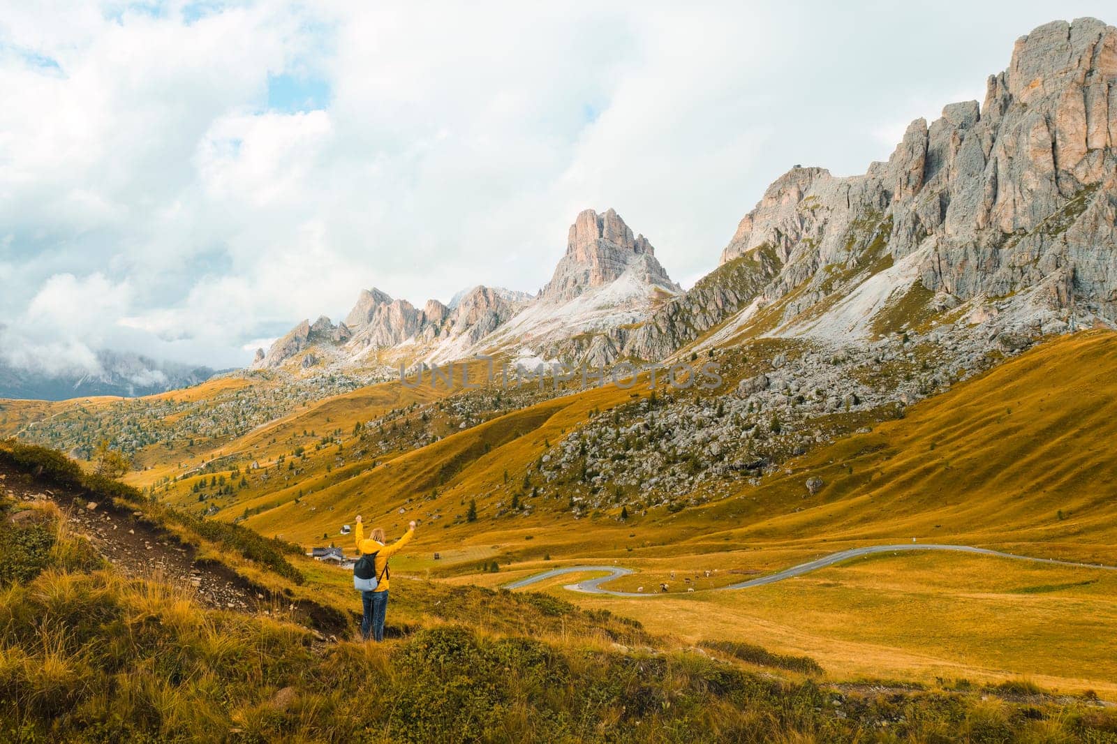 A hiker with outstretched arms, relishing the joy of exploration amidst the towering mountains of the renowned Giau Pass.