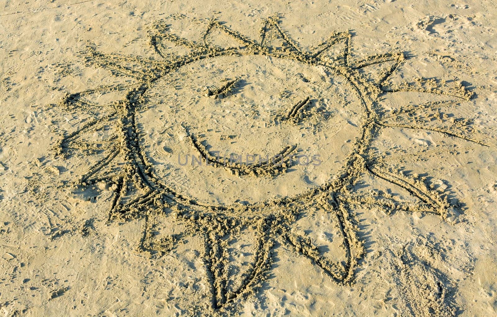 Child's drawing of smiling sun on the sand of Pacific ocean beach