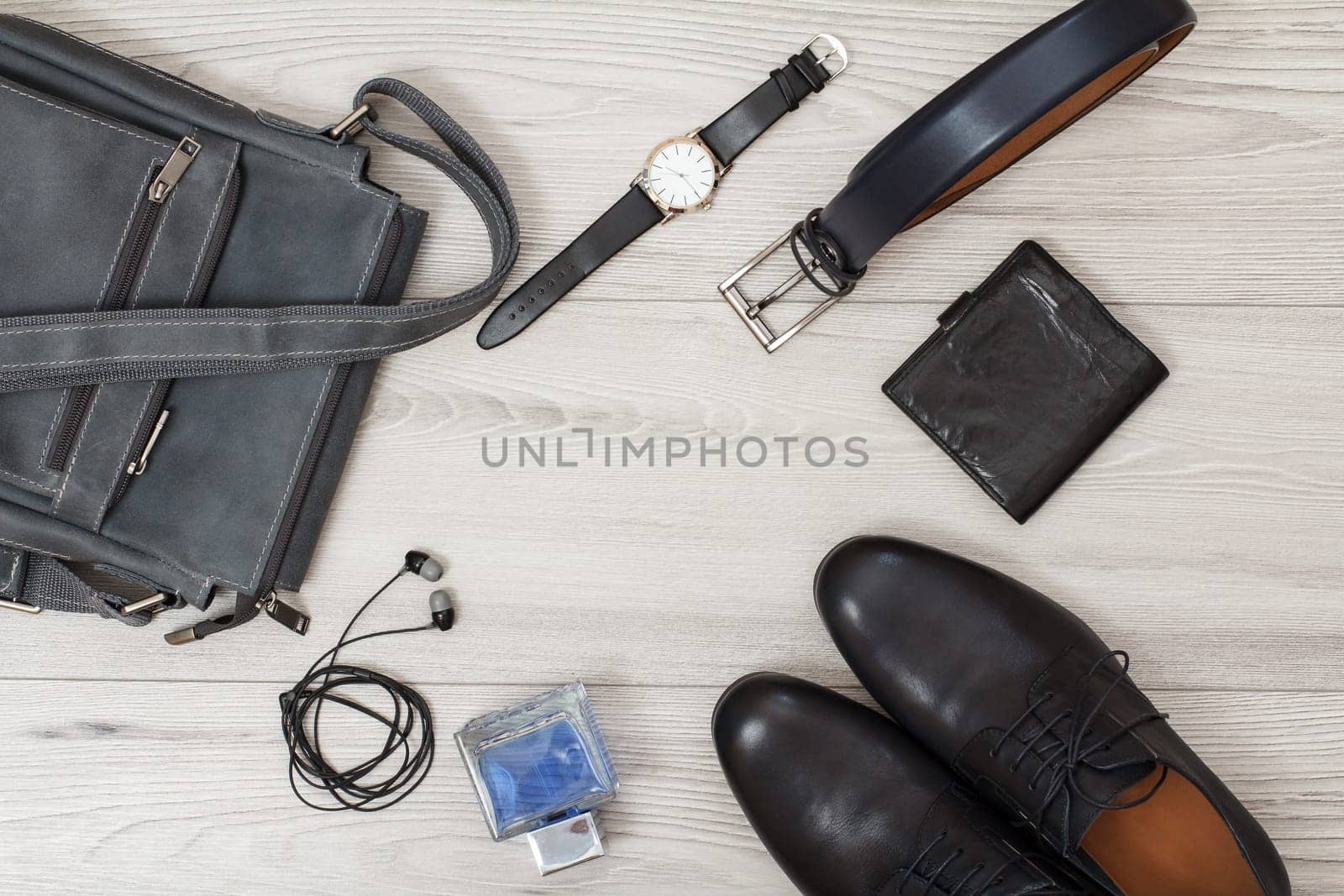 Pair of black leather men's shoes, leather shoulder bag for men, men's cologne, headphones, watch, belt and purse on gray wooden background. Men's accessories. Top view.
