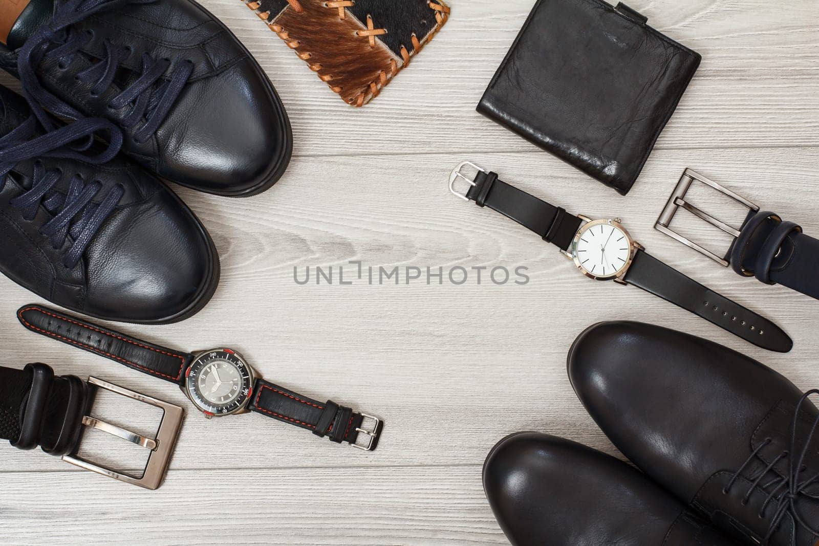 Two pairs of black leather men's shoes, two belts for men, wallets and wristwatches on gray wooden background. Men's accessories. Top view.