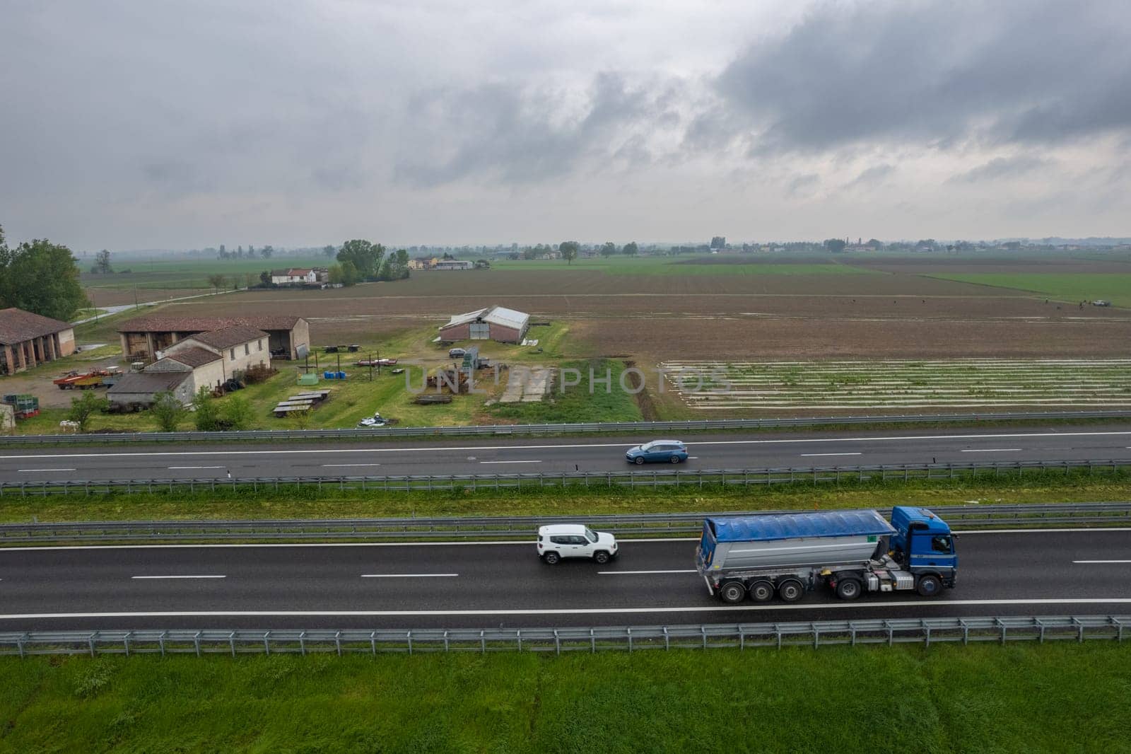 Piacenza, Italy - April 2023 Cargo trucks and cars in the motorway a1 autostrada del sole aerial point of view in between padain plain rural fields