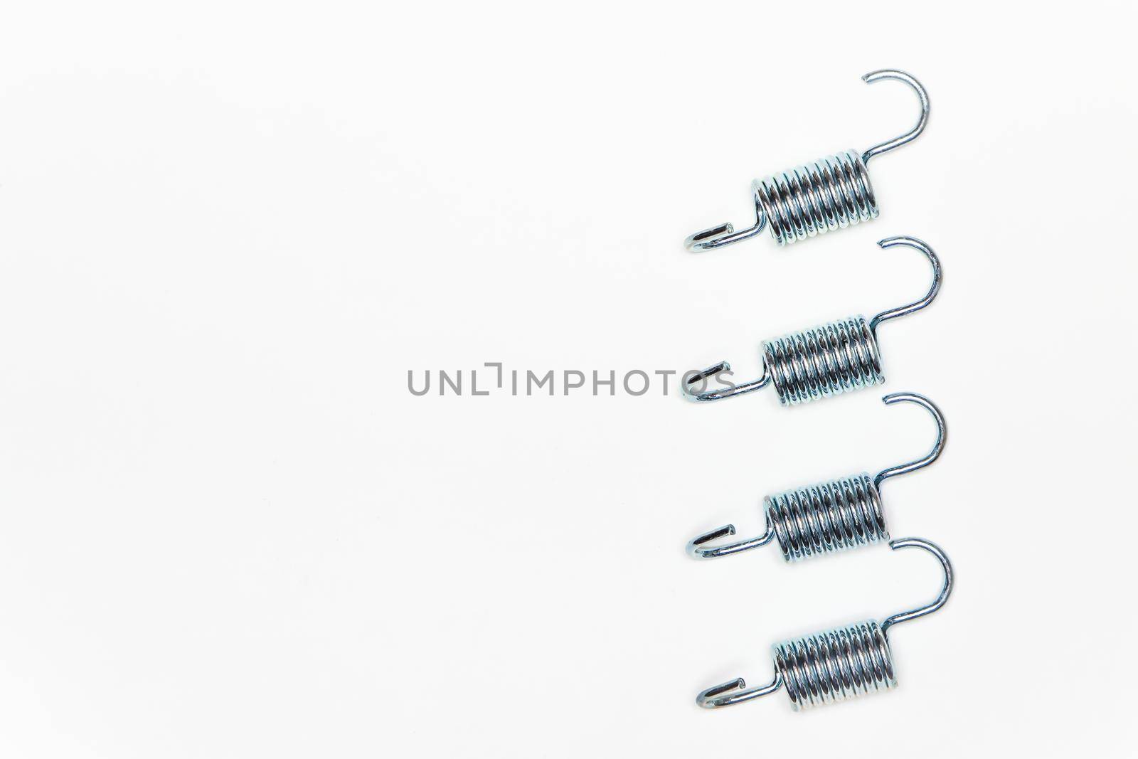 Four identical metal springs, parts for car repair. A set of spare parts for servicing vehicle calipers. Details on white background, copy space available.