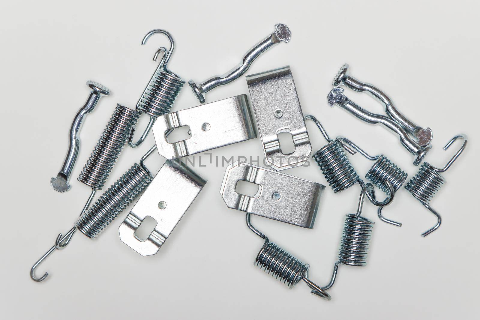 Metal fingers, plates, springs on the table, parts for car repair. A set of spare parts for servicing vehicle calipers. Details on white background, copy space available.