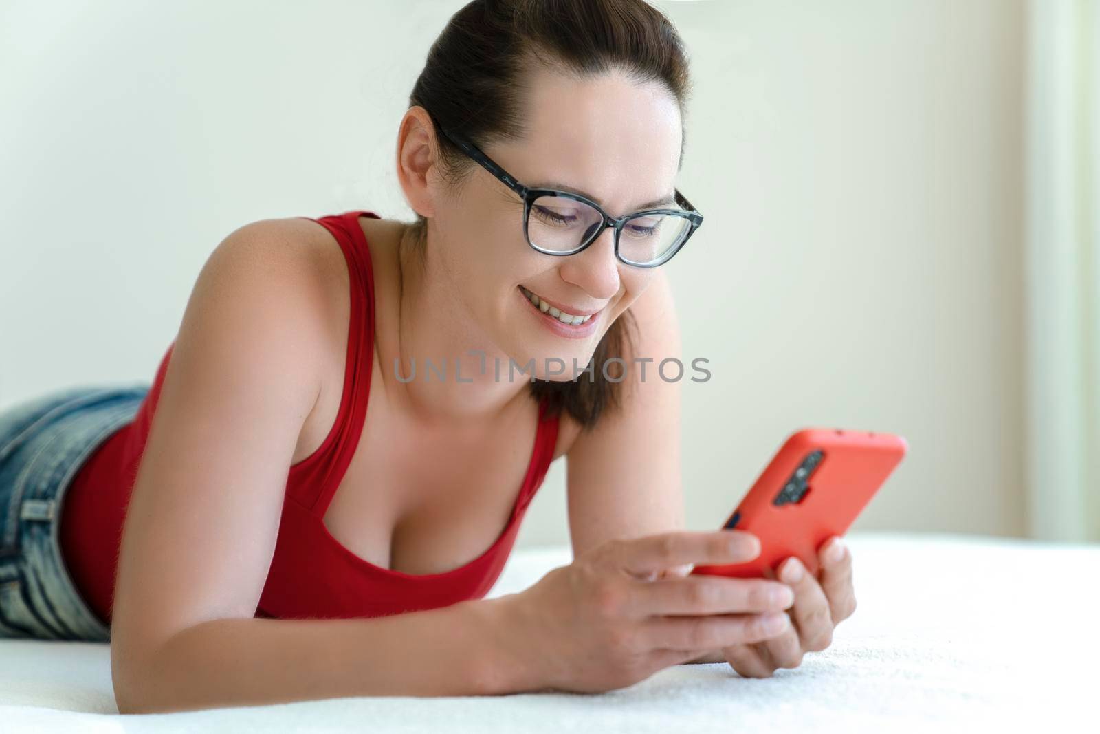 Woman talk via a smartphone video camera with positive emotions on her face while lying on bed.